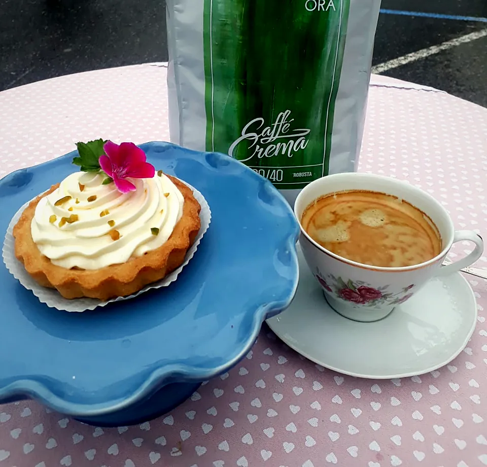 Eine Tasse Kaffee mit Crema neben einem Törtchen, dahinter die Canephora-Packung