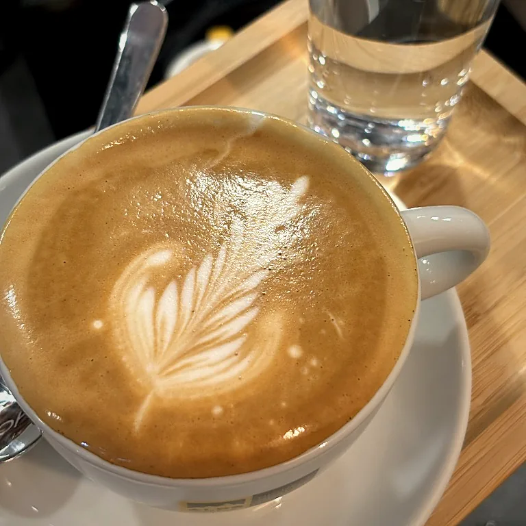 Cappuccino mit Latte-Art und ein Glas Wasser auf einem Holztablett